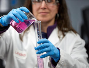 Femme technicienne de laboratoire, en blouse blanche et lunettes de protection, effectuant des tests. Elle tient un tube à essai contenant un liquide