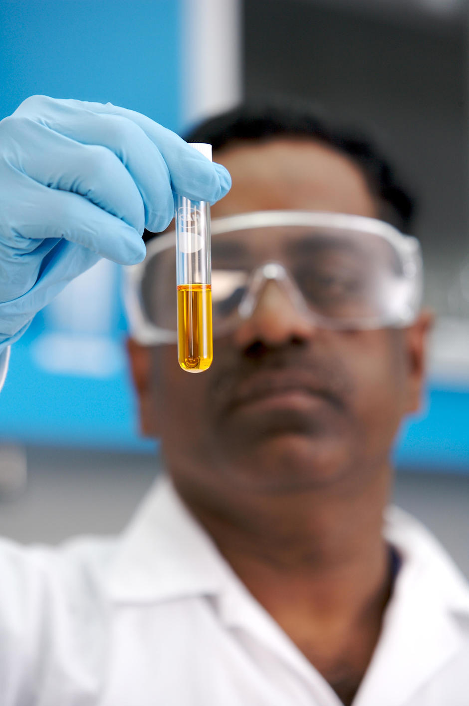 Laboratory employee wearing protection glasses and holding a vial lab with orange linquid inside.© Médiathèque VEOLIA - Eric Frotier de Bagneux